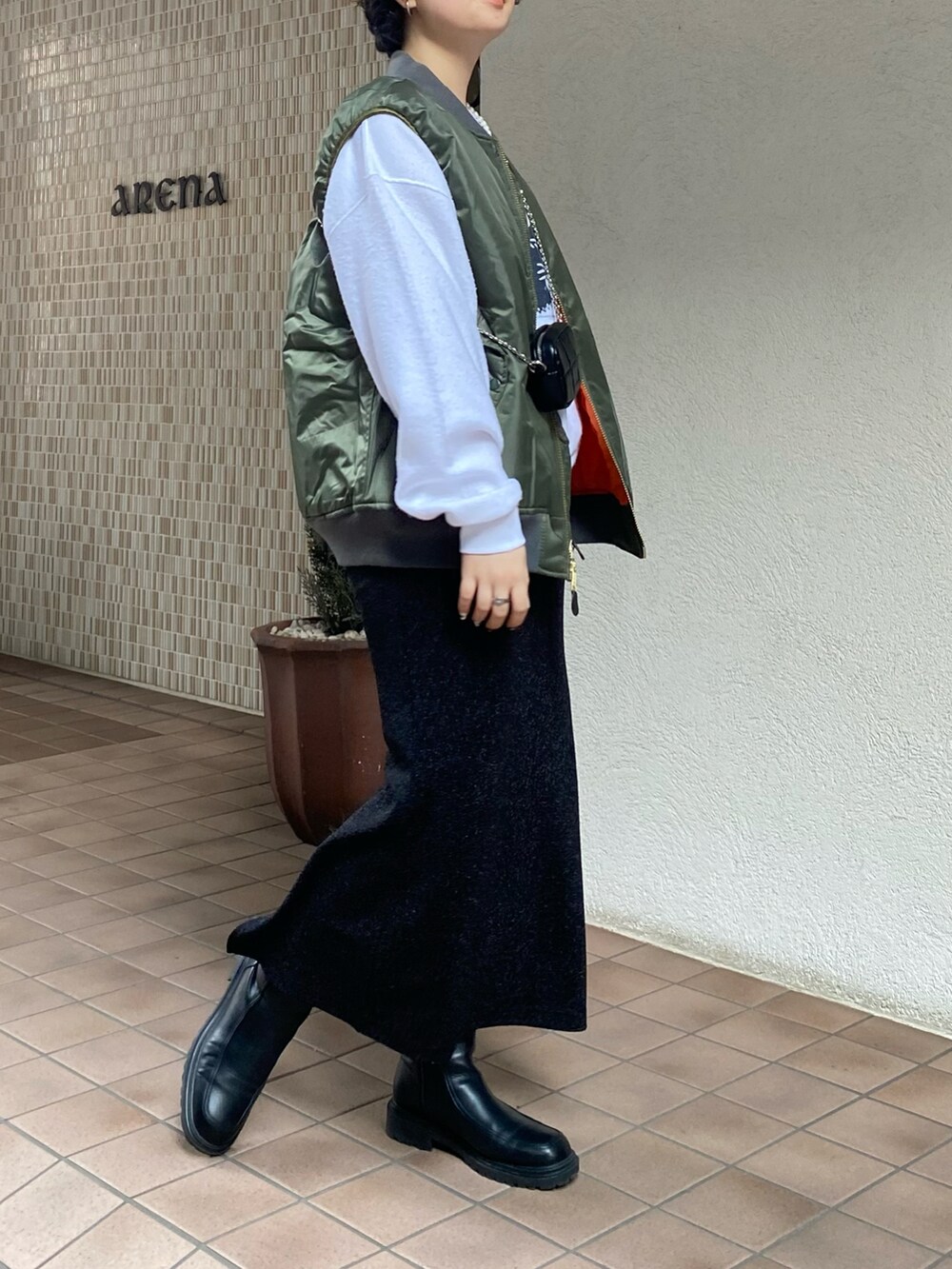 グリーン系のベスト、ブラック系のスカート、ホワイト系のスウェットを着用したレディースの冬コーディネートの3枚目の写真