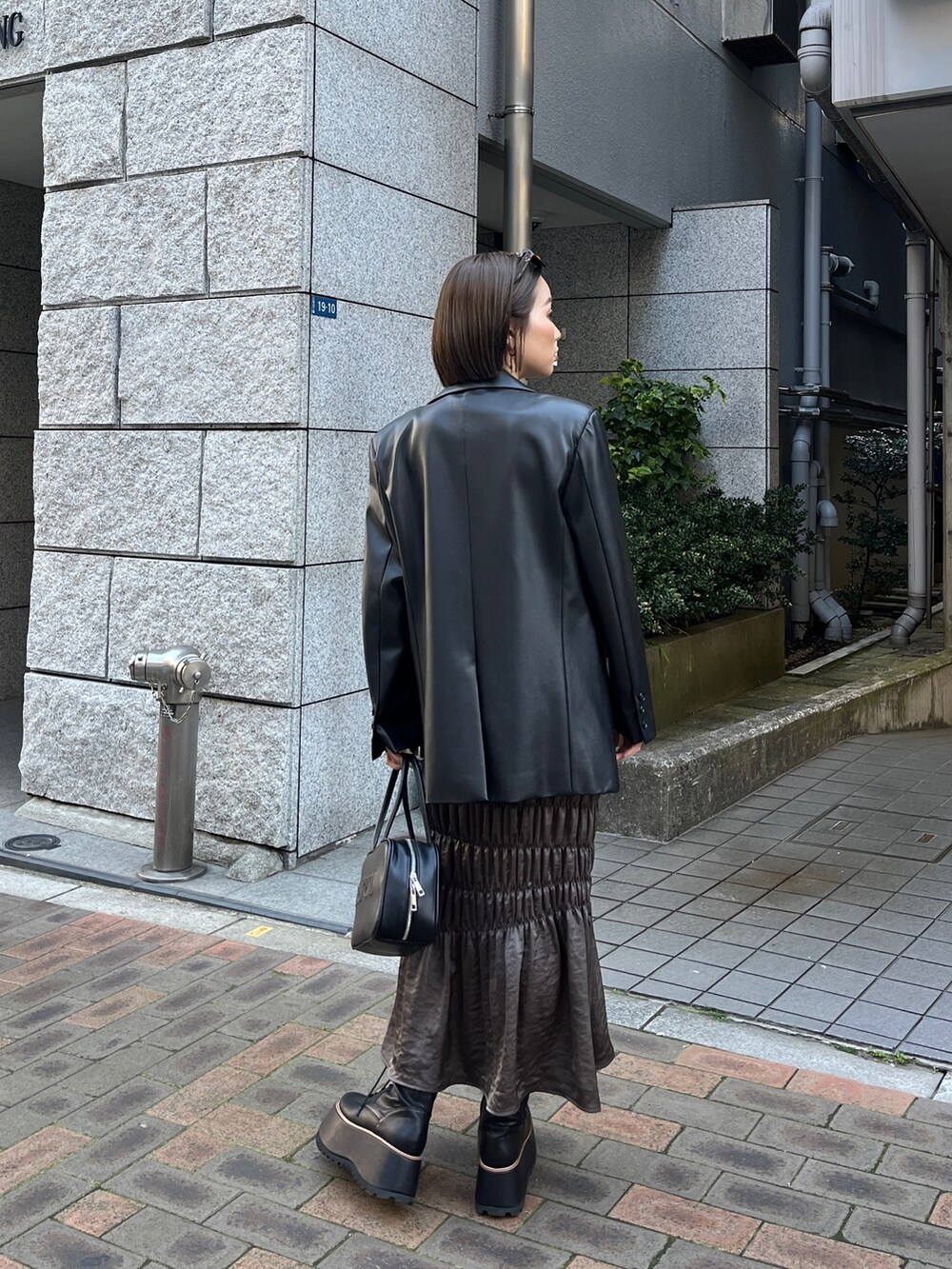 ブラック系のテーラードジャケット、ブラック系のニット/セーター、ブラウン系のスカートを着用したレディースの春コーディネートの2枚目の写真