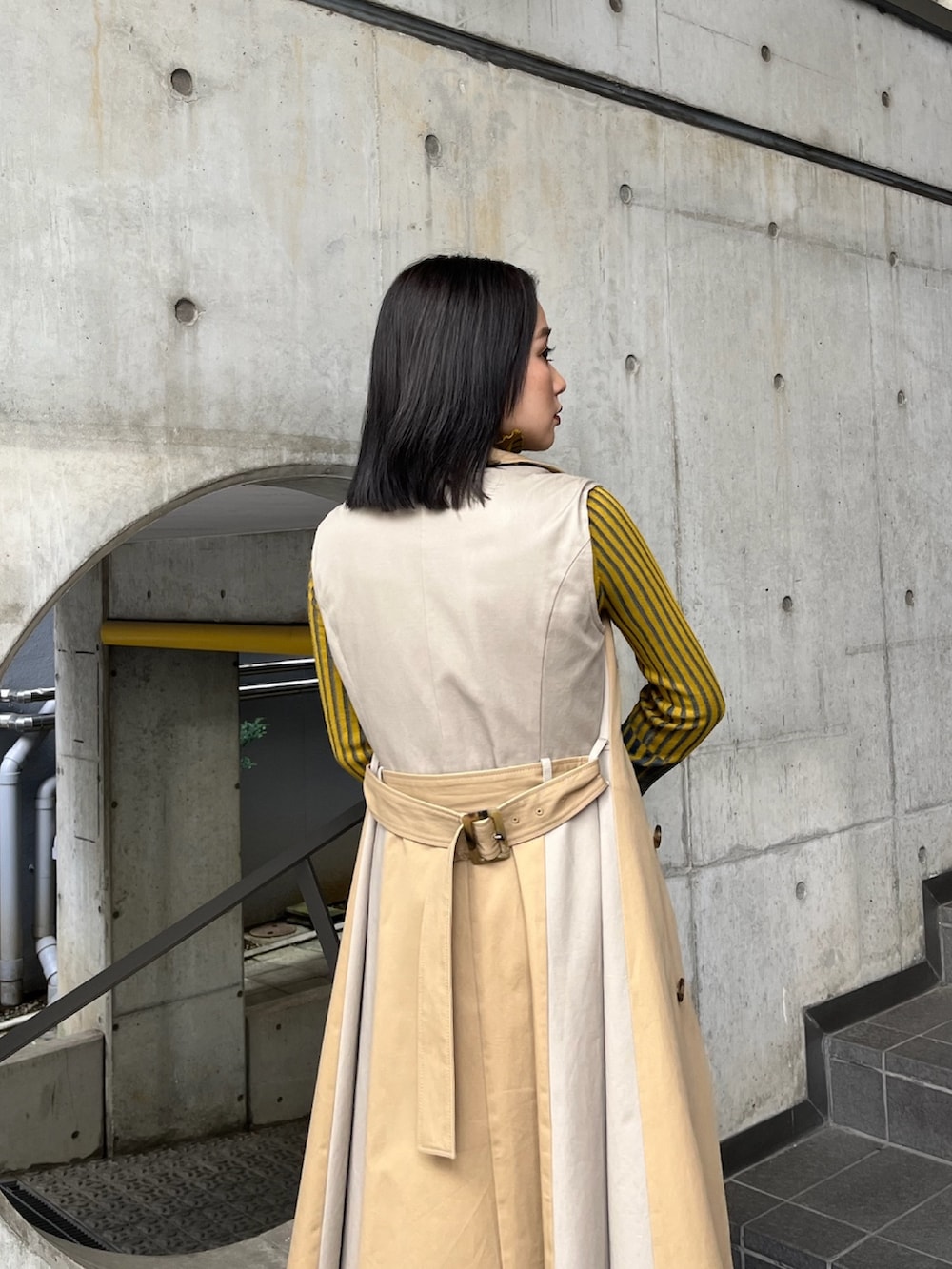 ベージュ系のトレンチコート、イエロー系のニット/セーター、ブラック系のスカートを着用したレディースの夏コーディネートの7枚目の写真