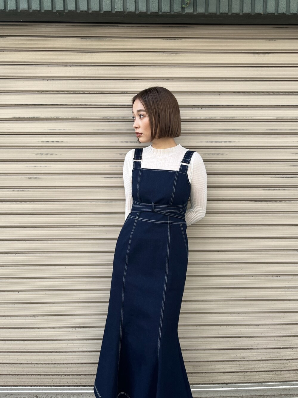 ブルー系のジャンパースカート、ホワイト系のニット/セーター、ホワイト系のブーツを着用したレディースの冬コーディネートの2枚目の写真