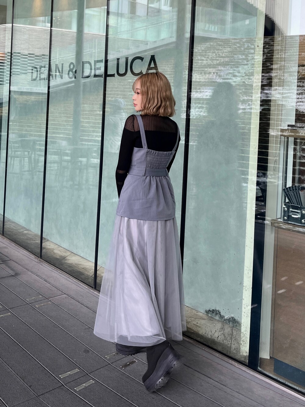 ブラック系のニット/セーター、グレー系のジャンパースカート、ブラック系のブーツを着用したレディースの春コーディネートの2枚目の写真