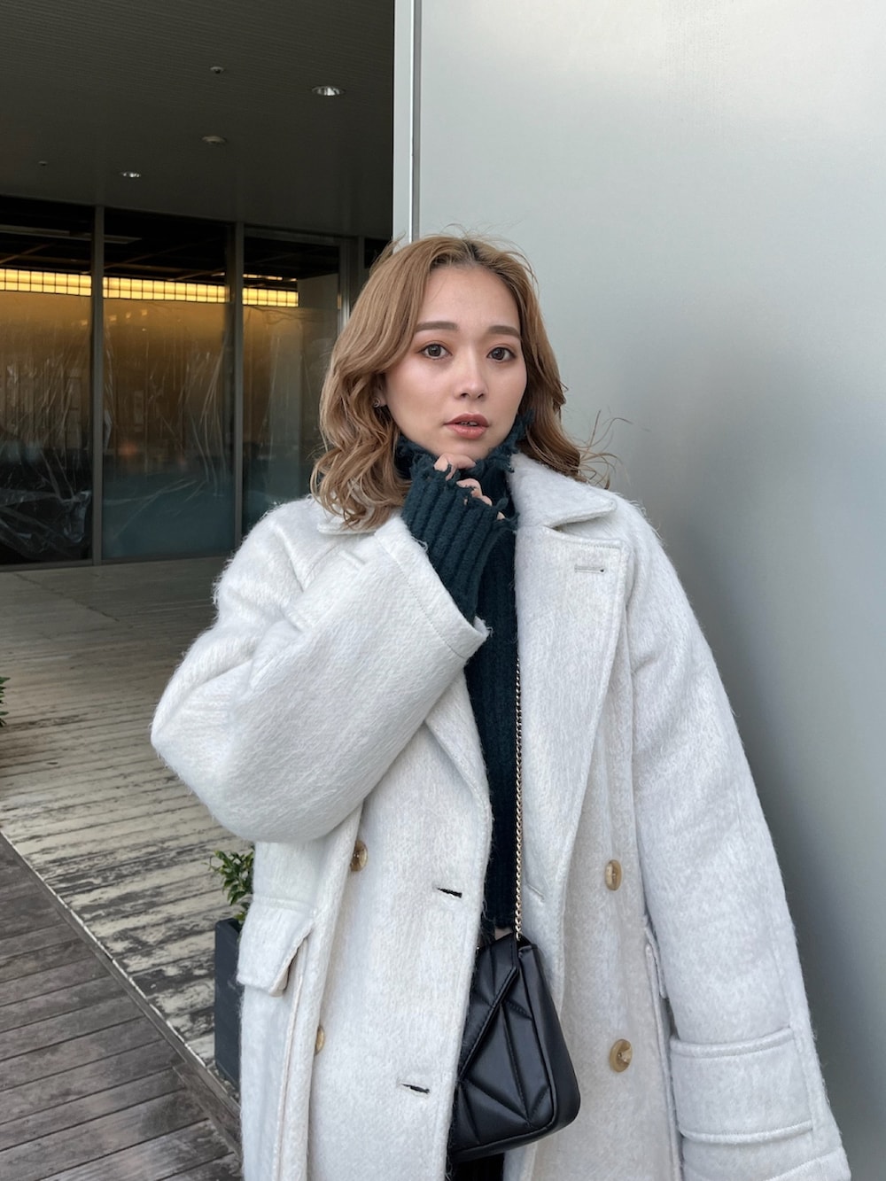 ホワイト系のチェスターコート、グリーン系のニット/セーター、ブラック系のブーツを着用したレディースの冬コーディネートの6枚目の写真