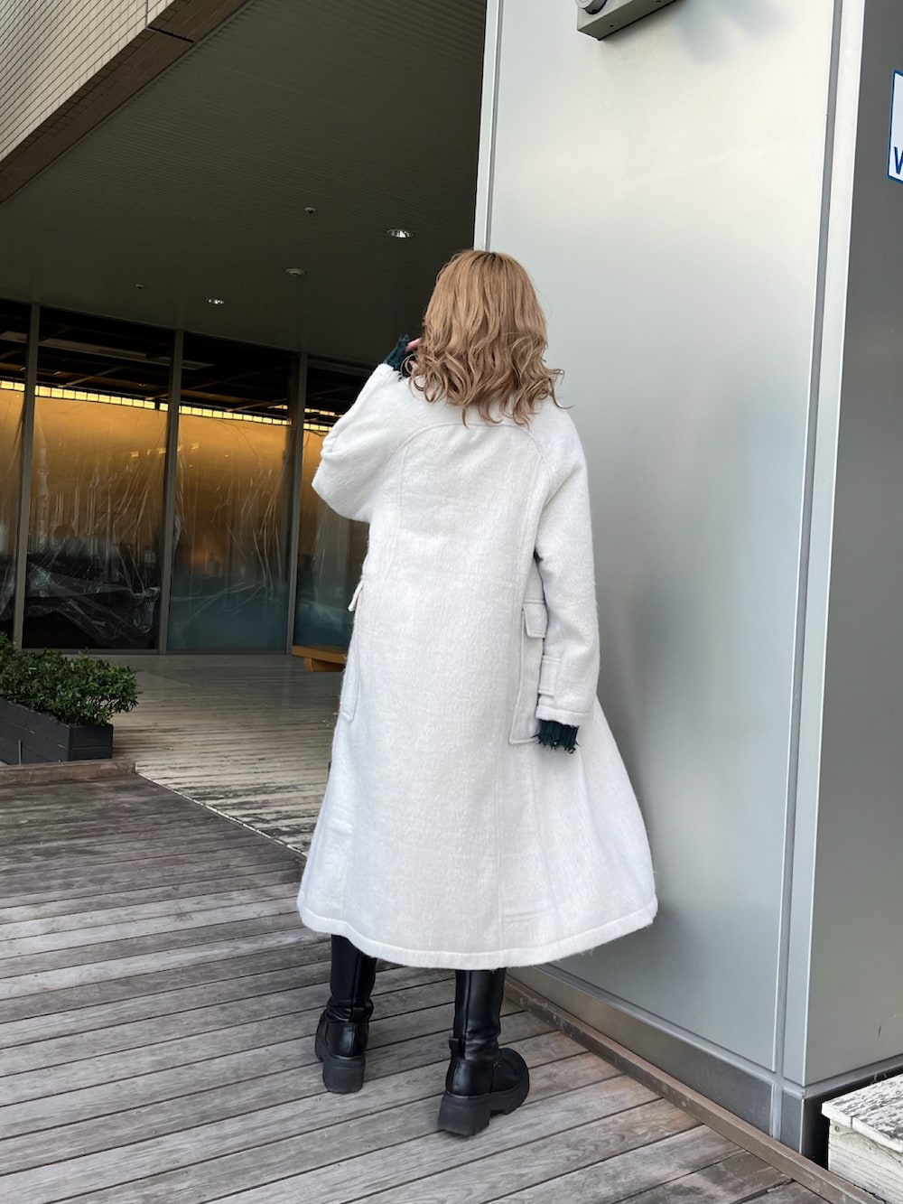 ホワイト系のチェスターコート、グリーン系のニット/セーター、ブラック系のブーツを着用したレディースの冬コーディネートの3枚目の写真