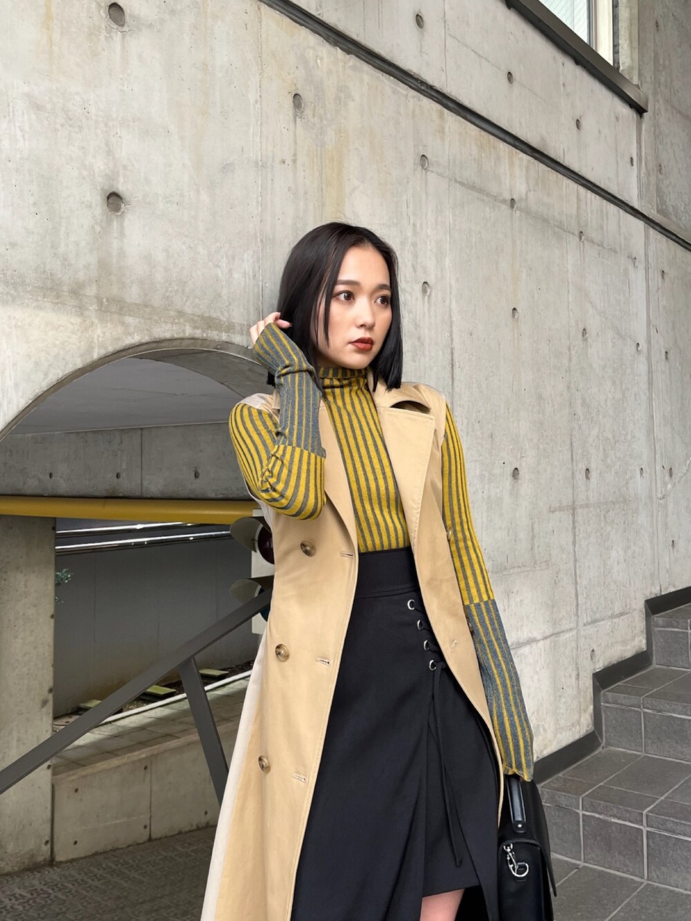 ベージュ系のトレンチコート、イエロー系のニット/セーター、ブラック系のスカートを着用したレディースの夏コーディネートの6枚目の写真