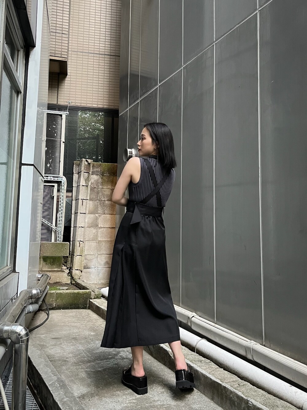 ブラック系のジャンパースカート、ブラック系のニット/セーター、ブラック系のサンダルを着用したレディースの夏コーディネートの2枚目の写真