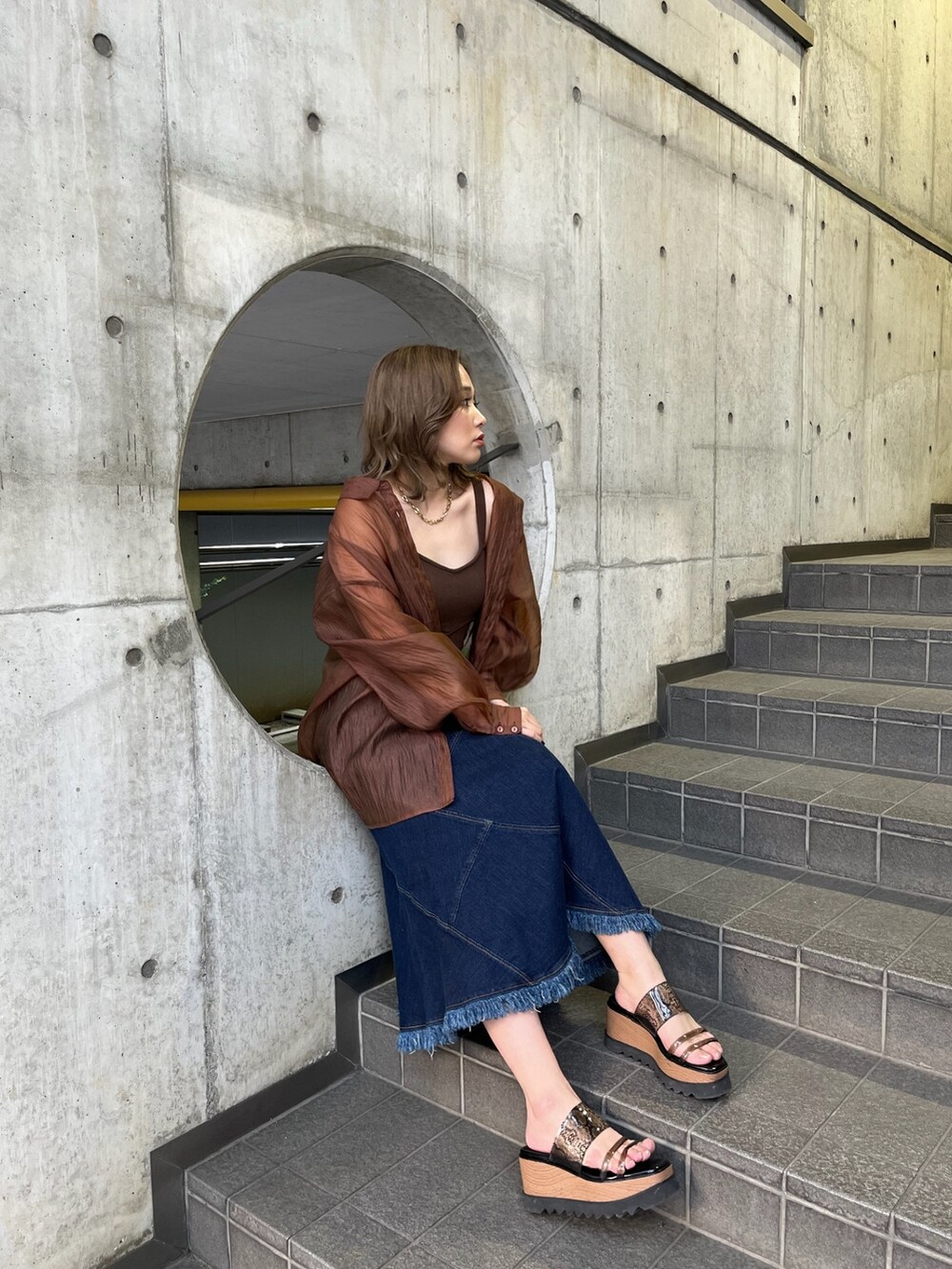 ブラウン系のシャツ/ブラウス、ブラウン系のニット/セーター、ブルー系のデニムスカートを着用したレディースの春コーディネートの2枚目の写真