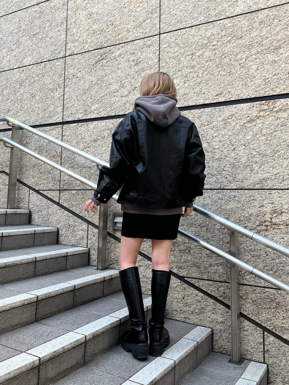 ブラック系のライダースジャケット、グレー系のパーカー、ブラック系のブーツを着用したレディースの秋コーディネートの2枚目の写真