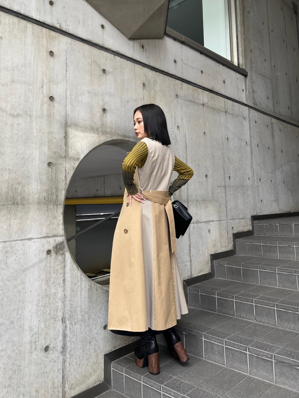 ベージュ系のトレンチコート、イエロー系のニット/セーター、ブラック系のスカートを着用したレディースの夏コーディネートの5枚目の写真