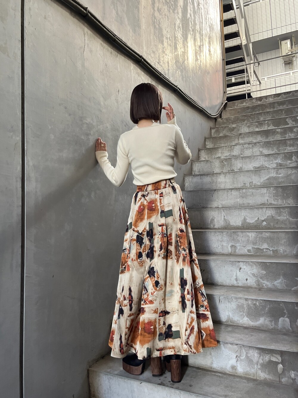 イエロー系のトレンチコート、ホワイト系のニット/セーター、オレンジ系のスカートを着用したレディースの秋コーディネートの7枚目の写真