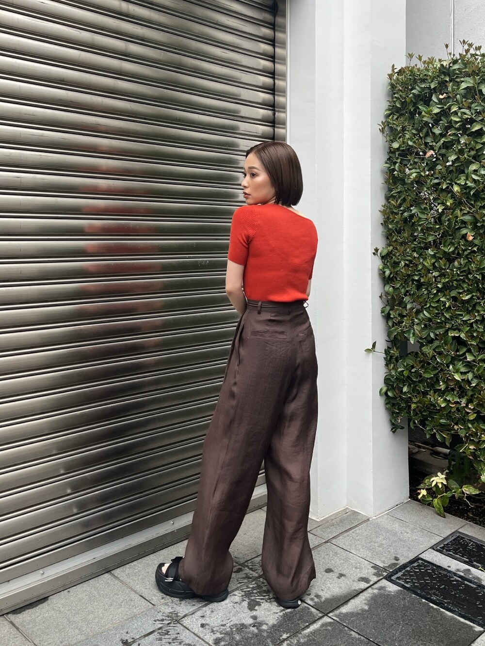 オレンジ系のニット/セーター、ブラウン系のその他パンツ、ブラック系のサンダルを着用したレディースの夏コーディネートの3枚目の写真