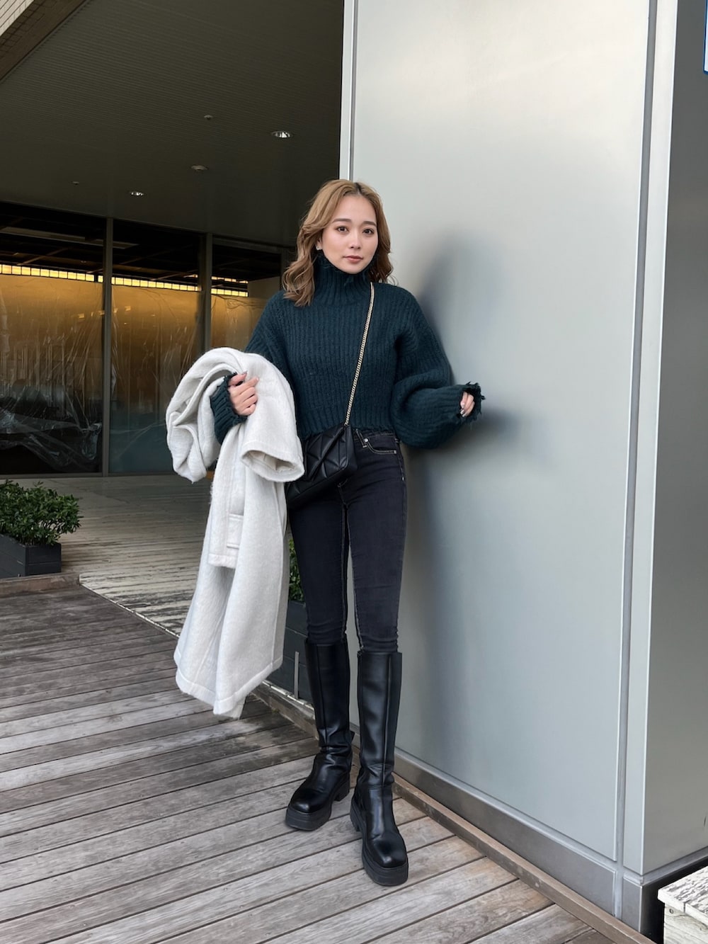 ホワイト系のチェスターコート、グリーン系のニット/セーター、ブラック系のブーツを着用したレディースの冬コーディネートの4枚目の写真