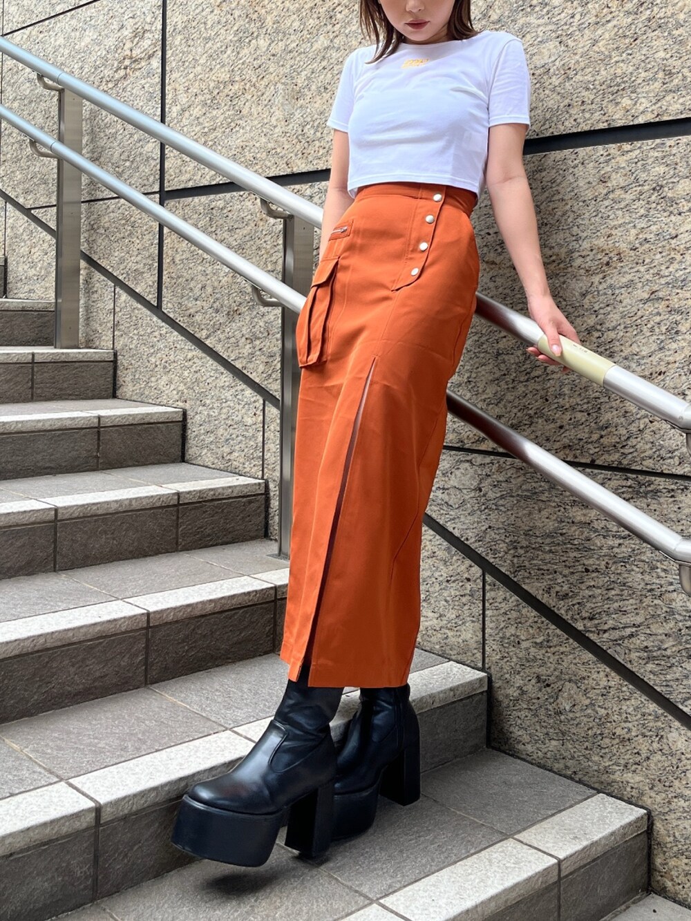 ホワイト系のTシャツ/カットソー、オレンジ系のスカート、ブラック系のブーツを着用したレディースの夏コーディネートの2枚目の写真