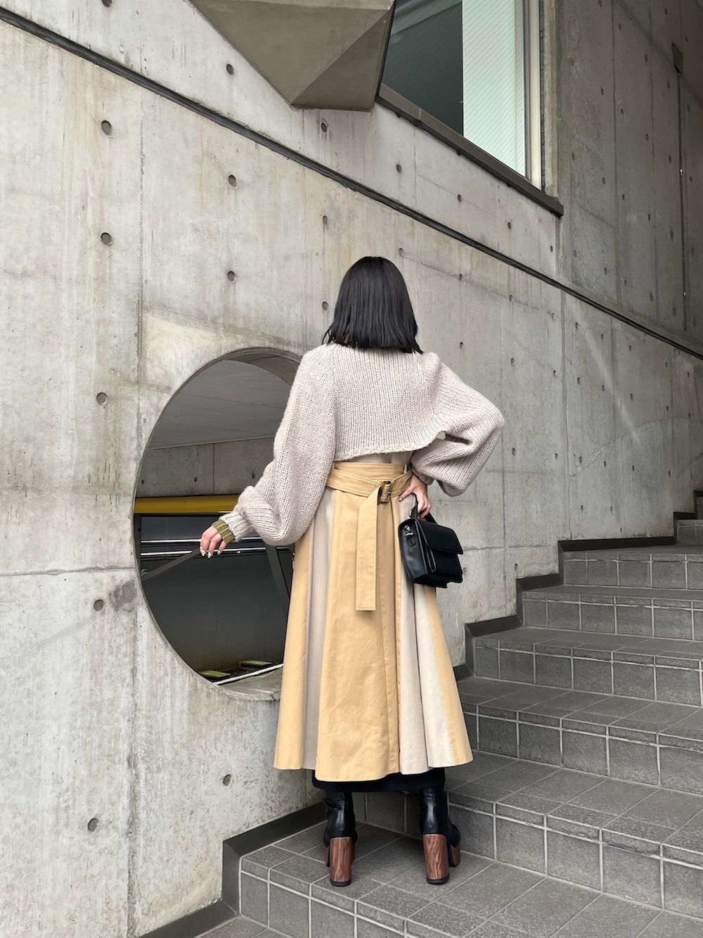 ベージュ系のトレンチコート、イエロー系のニット/セーター、ブラック系のスカートを着用したレディースの夏コーディネートの2枚目の写真
