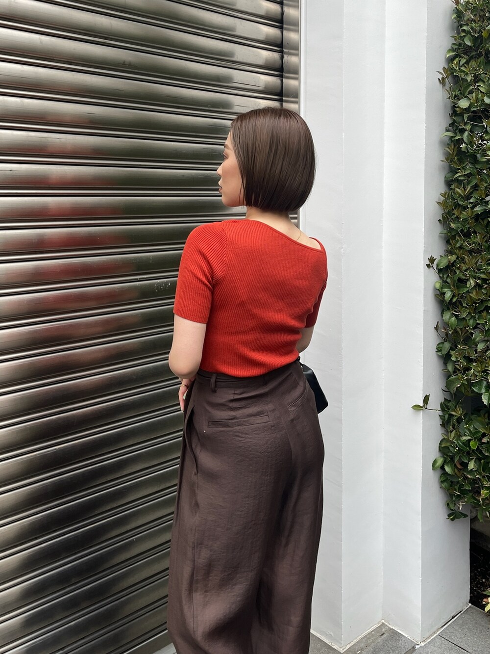 オレンジ系のニット/セーター、ブラウン系のその他パンツ、ブラック系のサンダルを着用したレディースの夏コーディネートの6枚目の写真