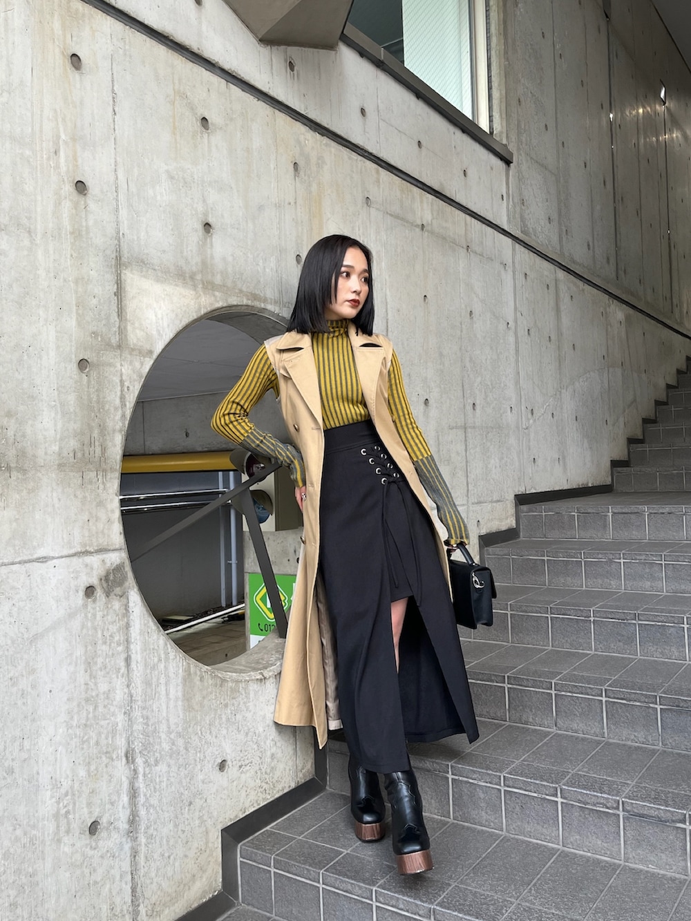 ベージュ系のトレンチコート、イエロー系のニット/セーター、ブラック系のスカートを着用したレディースの夏コーディネートの4枚目の写真