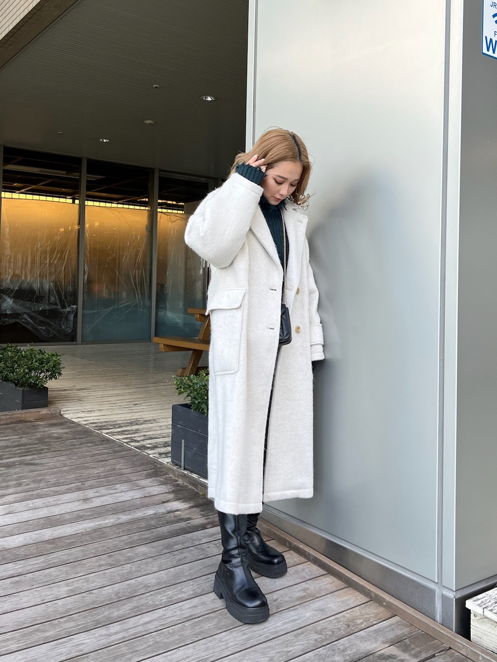 ホワイト系のチェスターコート、グリーン系のニット/セーター、ブラック系のブーツを着用したレディースの冬コーディネートの2枚目の写真