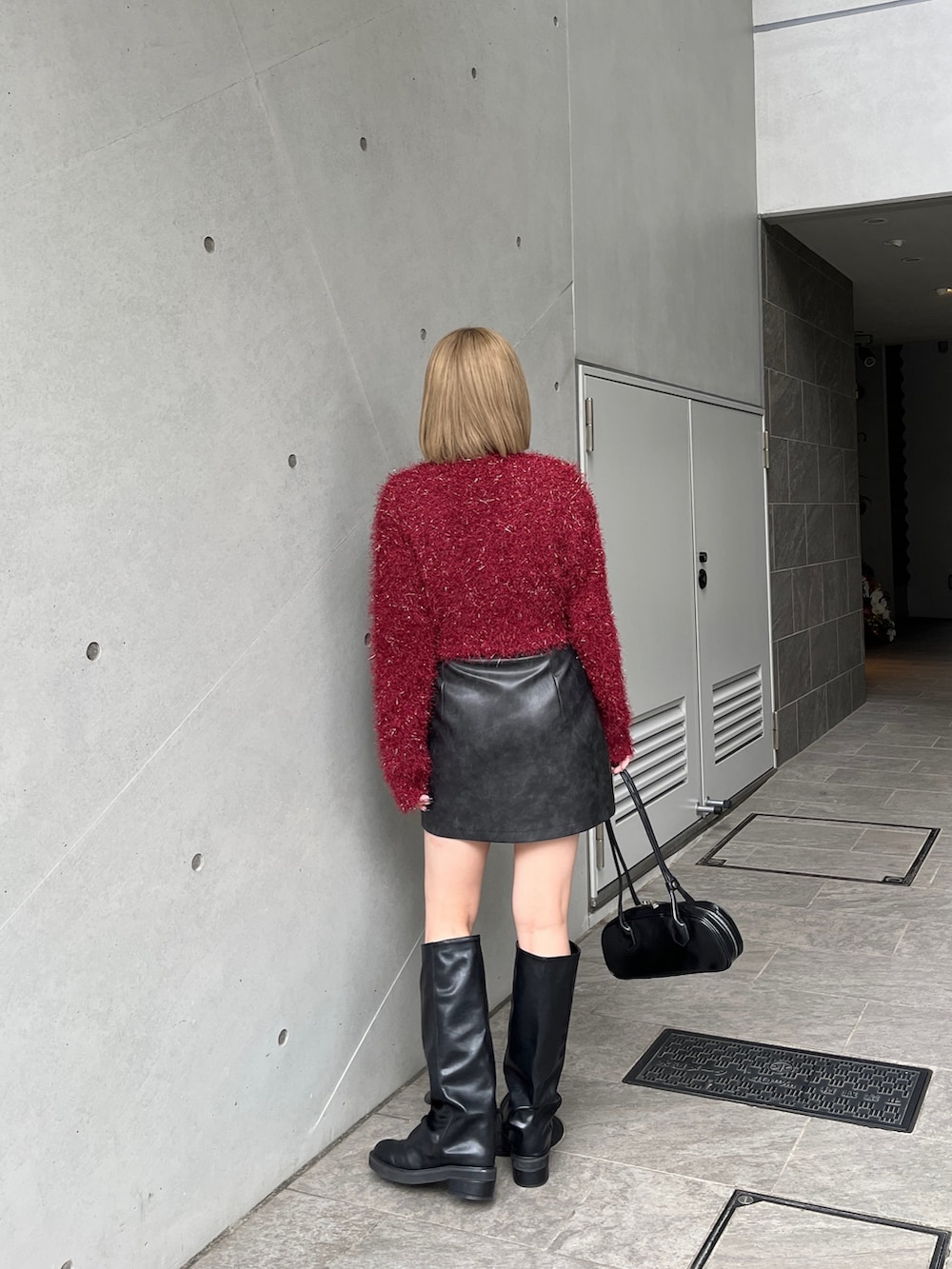 レッド系のニット/セーター、ブラウン系のスカート、ブラック系のブーツを着用したレディースの冬コーディネートの2枚目の写真