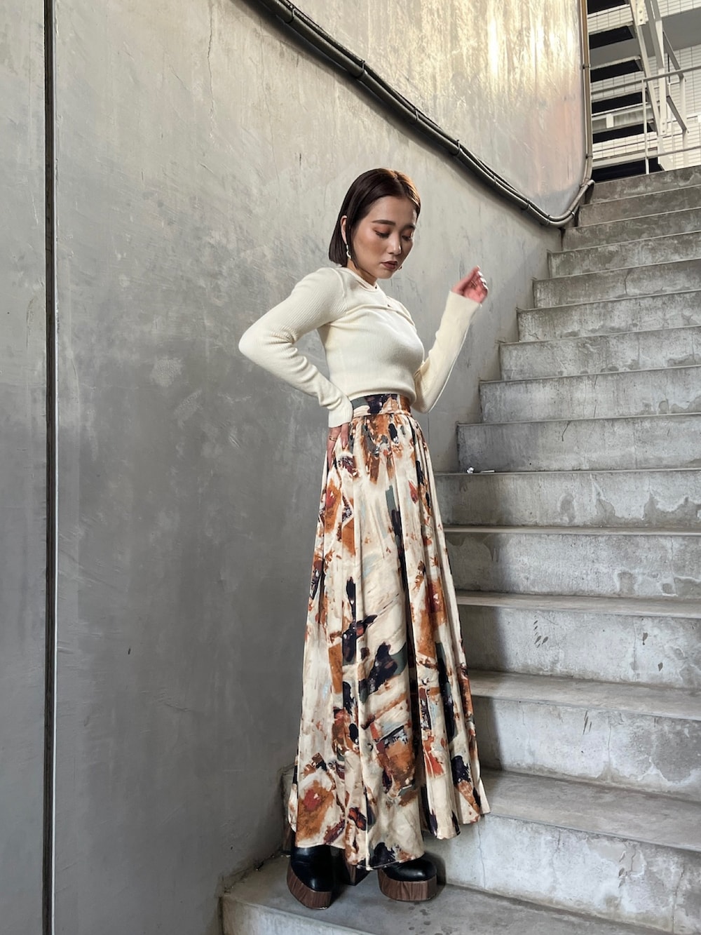 イエロー系のトレンチコート、ホワイト系のニット/セーター、オレンジ系のスカートを着用したレディースの秋コーディネートの6枚目の写真