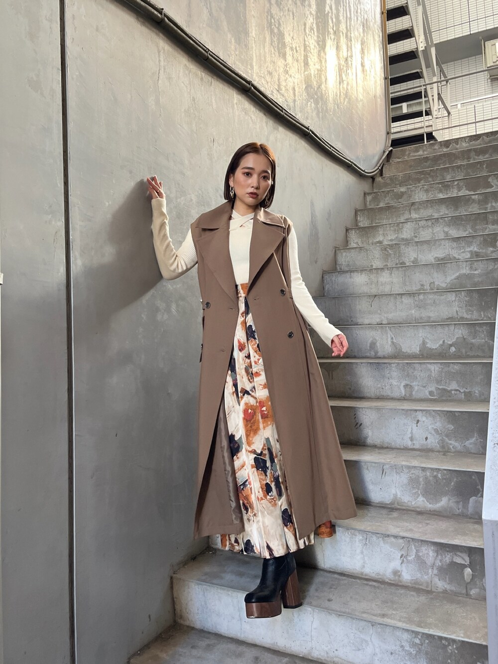 イエロー系のトレンチコート、ホワイト系のニット/セーター、オレンジ系のスカートを着用したレディースの秋コーディネートの2枚目の写真