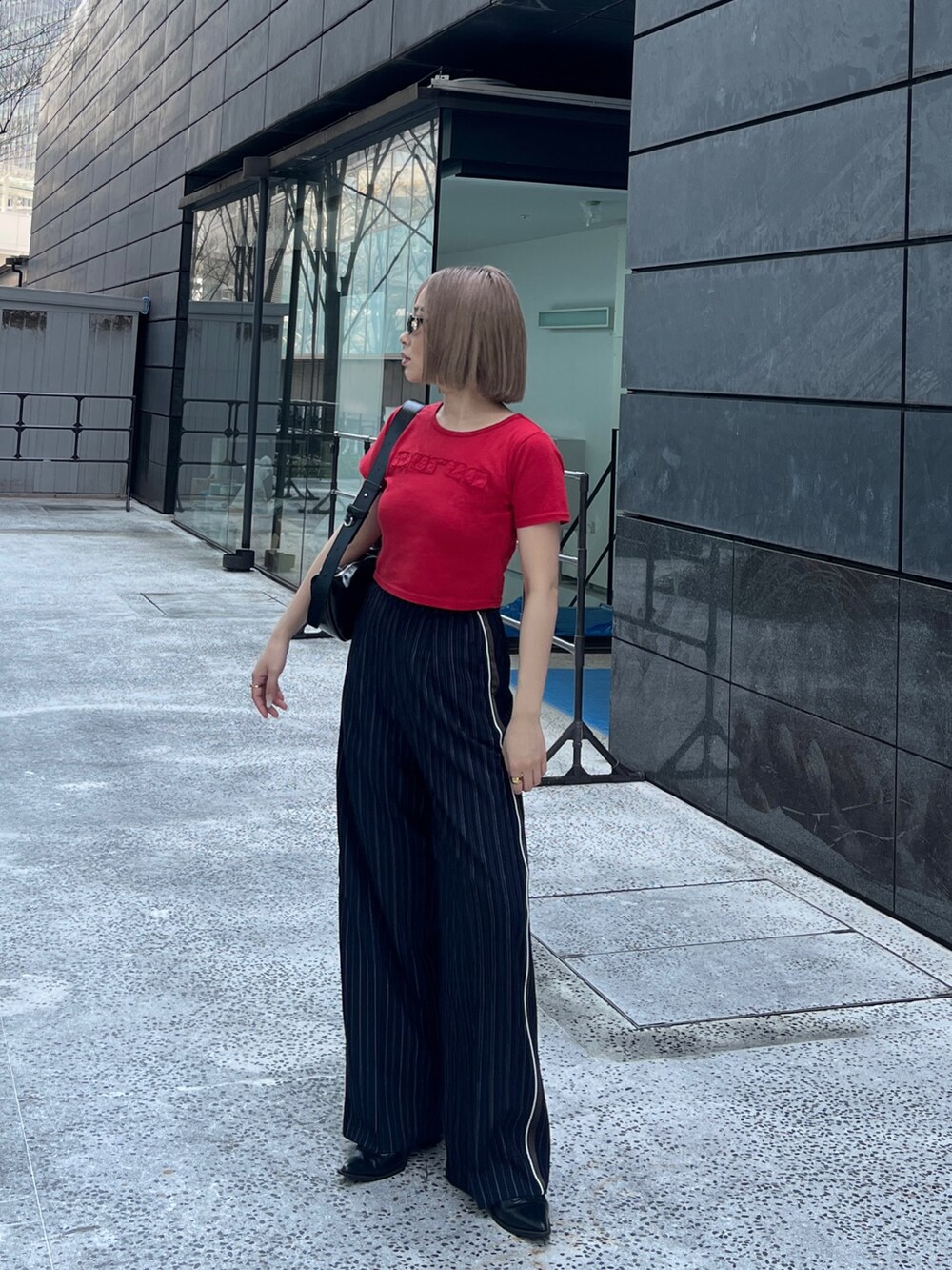 レッド系のTシャツ/カットソー、ブルー系のスラックス、ブラック系のショルダーバッグを着用したレディースの春コーディネートの2枚目の写真