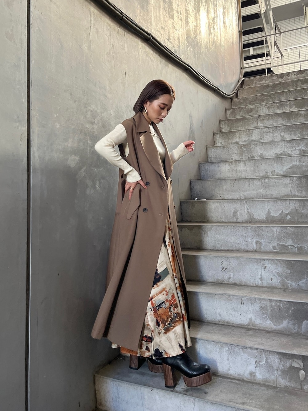 イエロー系のトレンチコート、ホワイト系のニット/セーター、オレンジ系のスカートを着用したレディースの秋コーディネートの3枚目の写真