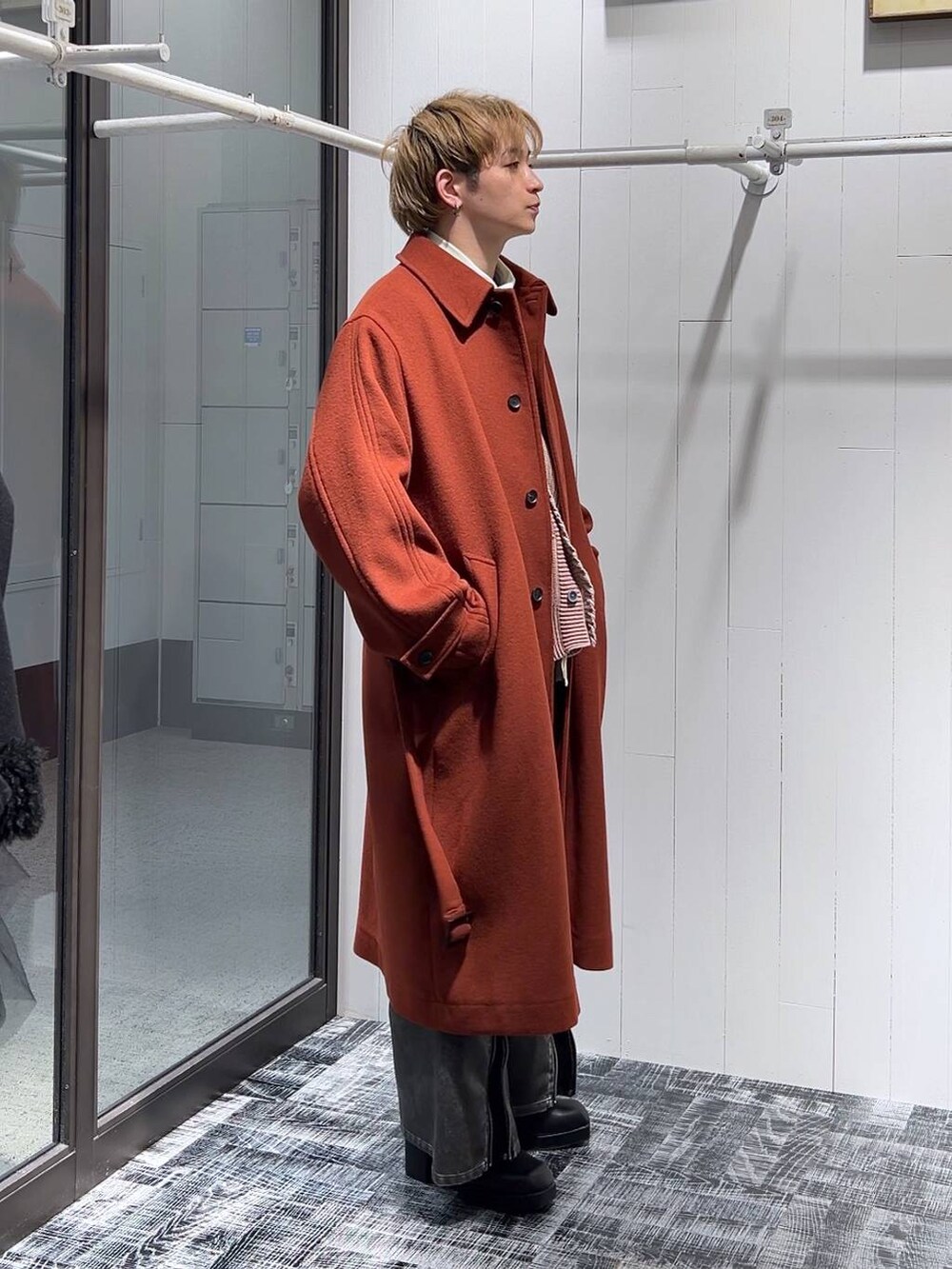 オレンジ系のステンカラーコート、グレー系のカーゴパンツ、ピンク系のカーディガン/ボレロを着用したメンズの冬コーディネートの2枚目の写真