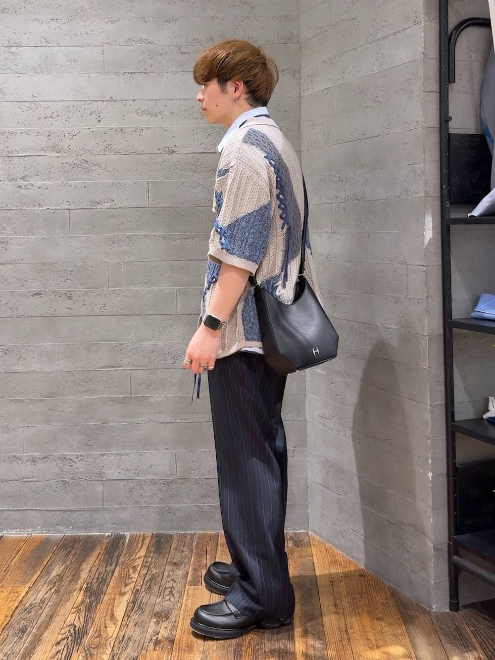 ブルー系のスラックス、ブラック系のドレスシューズ、ブラック系のショルダーバッグを着用したメンズの春コーディネートの3枚目の写真