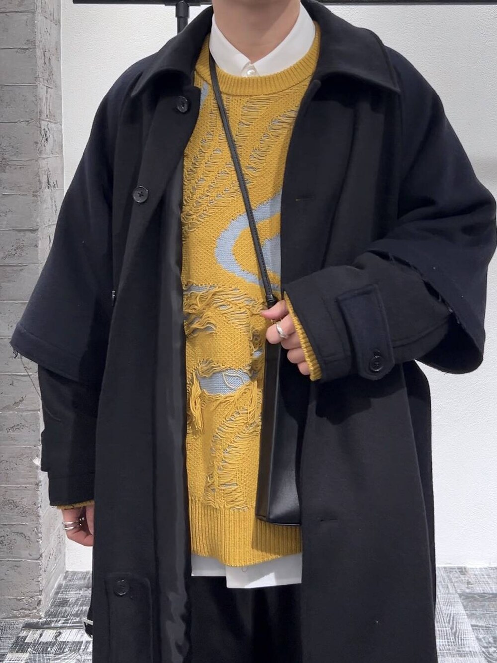 イエロー系のニット/セーター、ブラック系のショルダーバッグ、ブラック系のドレスシューズを着用したメンズの冬コーディネートの5枚目の写真