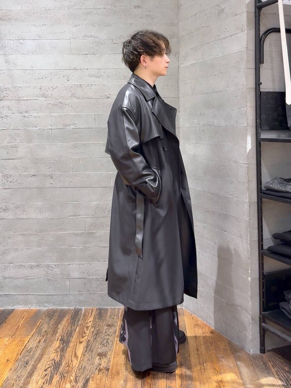 ブラック系のトレンチコート、ブラック系のブーツ、シルバー系のネックレスを着用したメンズの秋コーディネートの2枚目の写真