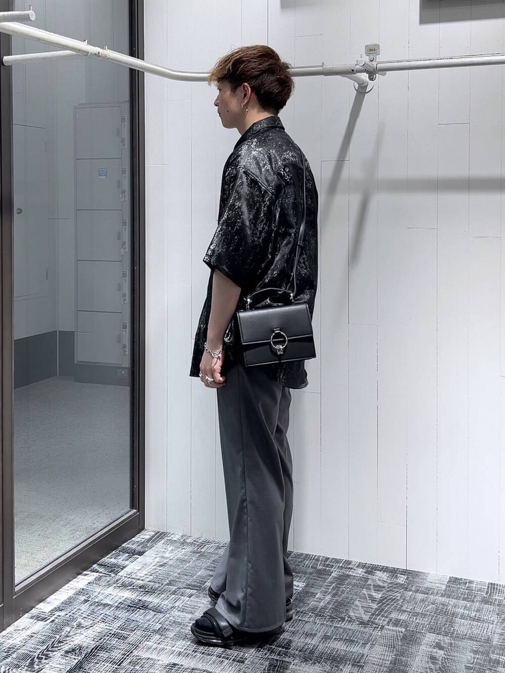 グレー系のスラックス、ブラック系のショルダーバッグ、ブラック系のサンダルを着用したメンズの夏コーディネートの3枚目の写真