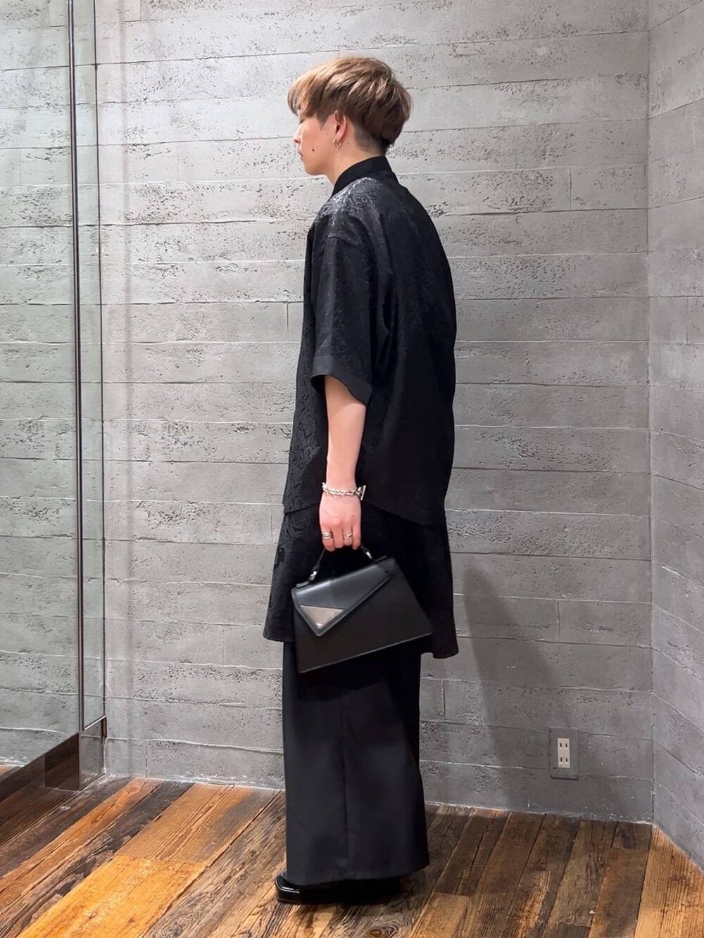 ブラック系のスラックス、ブラック系のハンドバッグ、ブラック系のサンダルを着用したメンズの夏コーディネートの4枚目の写真