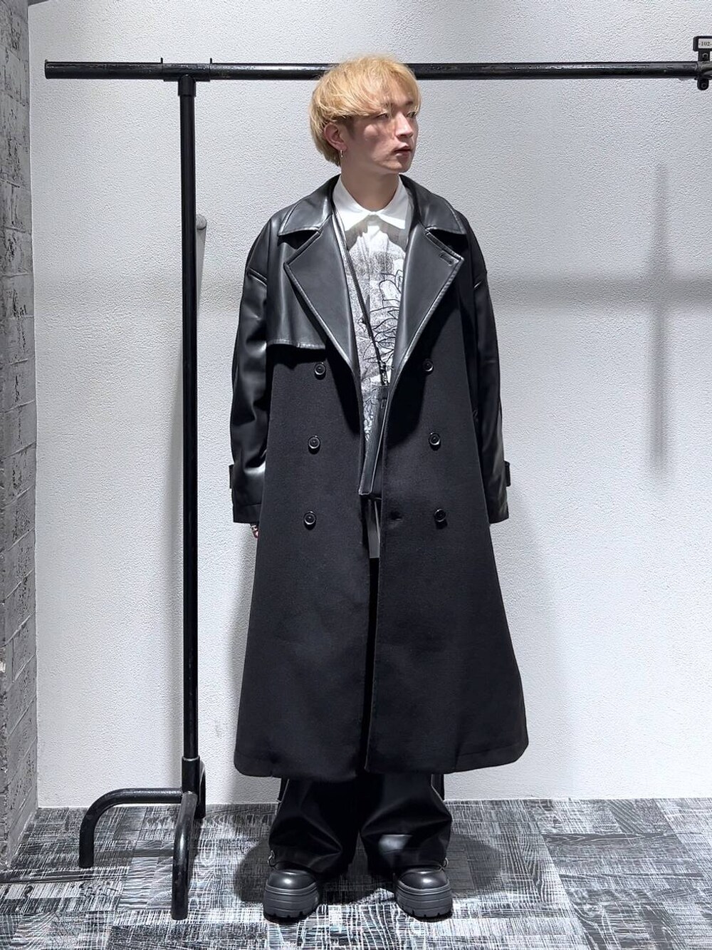 ブラック系のトレンチコート、ブラック系のショルダーバッグ、ブラック系のブーツを着用したメンズの秋コーディネートの2枚目の写真