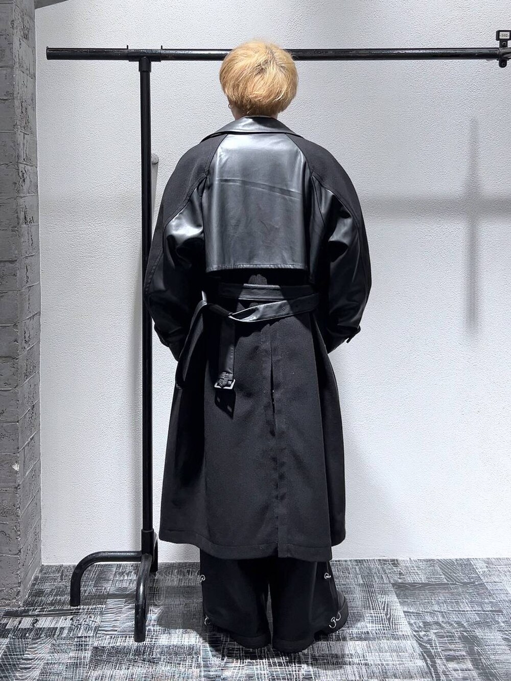 ブラック系のトレンチコート、ブラック系のショルダーバッグ、ブラック系のブーツを着用したメンズの秋コーディネートの3枚目の写真