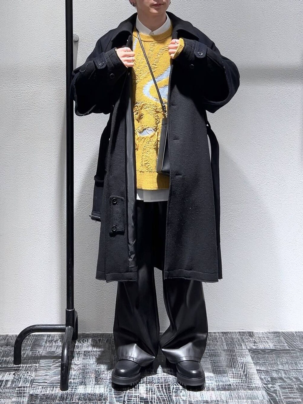 イエロー系のニット/セーター、ブラック系のショルダーバッグ、ブラック系のドレスシューズを着用したメンズの冬コーディネートの2枚目の写真