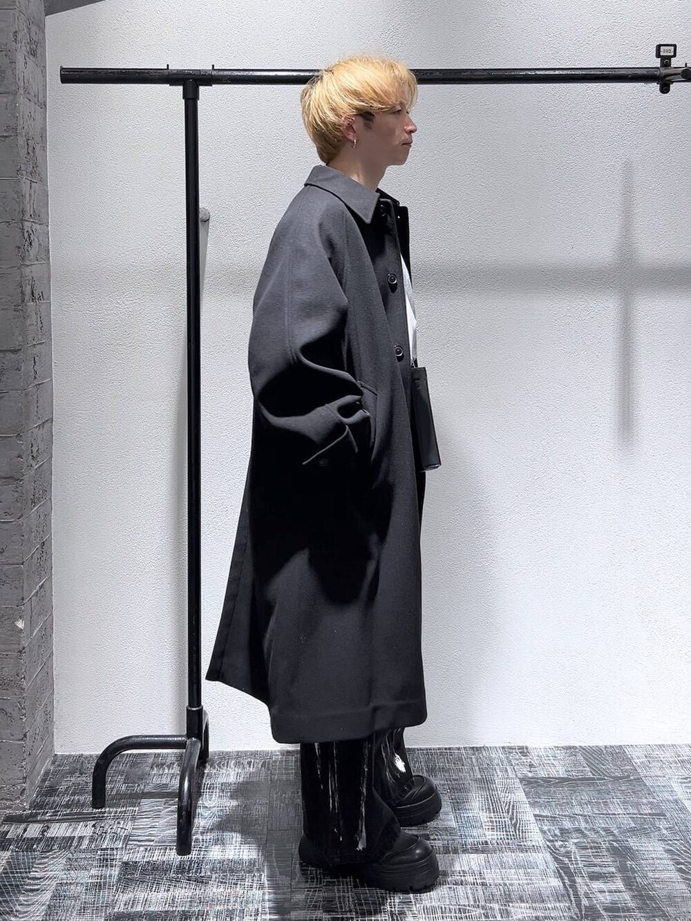 ブラック系のステンカラーコート、グレー系のスウェット、ブラック系のブーツを着用したメンズの冬コーディネートの3枚目の写真