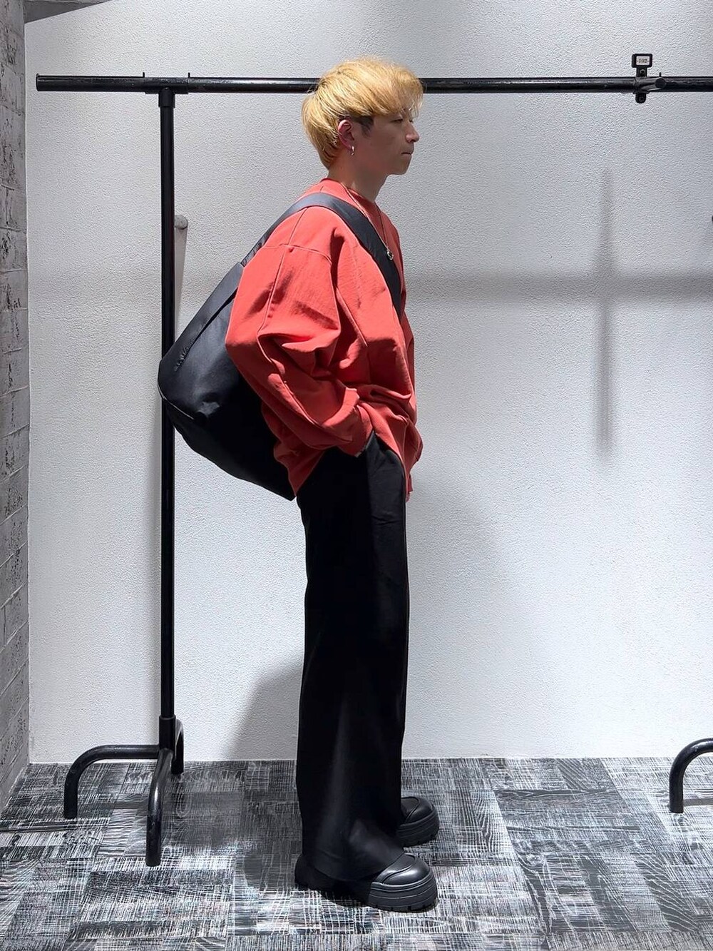 ブラック系のショルダーバッグ、オレンジ系のスウェット、ブラック系のブーツを着用したメンズの冬コーディネートの2枚目の写真