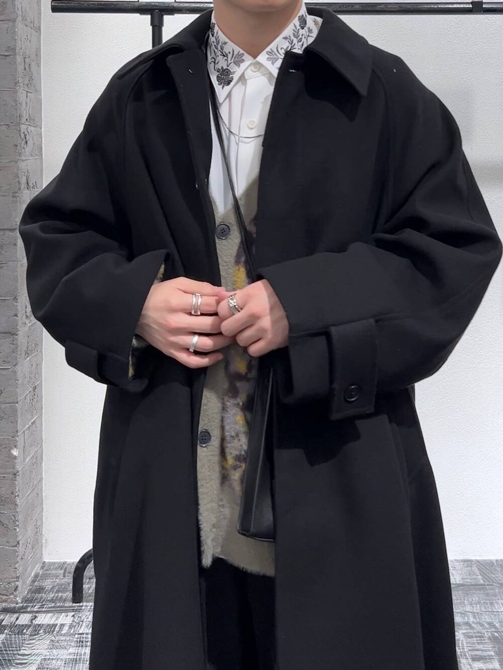 ブラック系のステンカラーコート、ブラック系のショルダーバッグ、グレー系のカーディガン/ボレロを着用したメンズの冬コーディネートの5枚目の写真