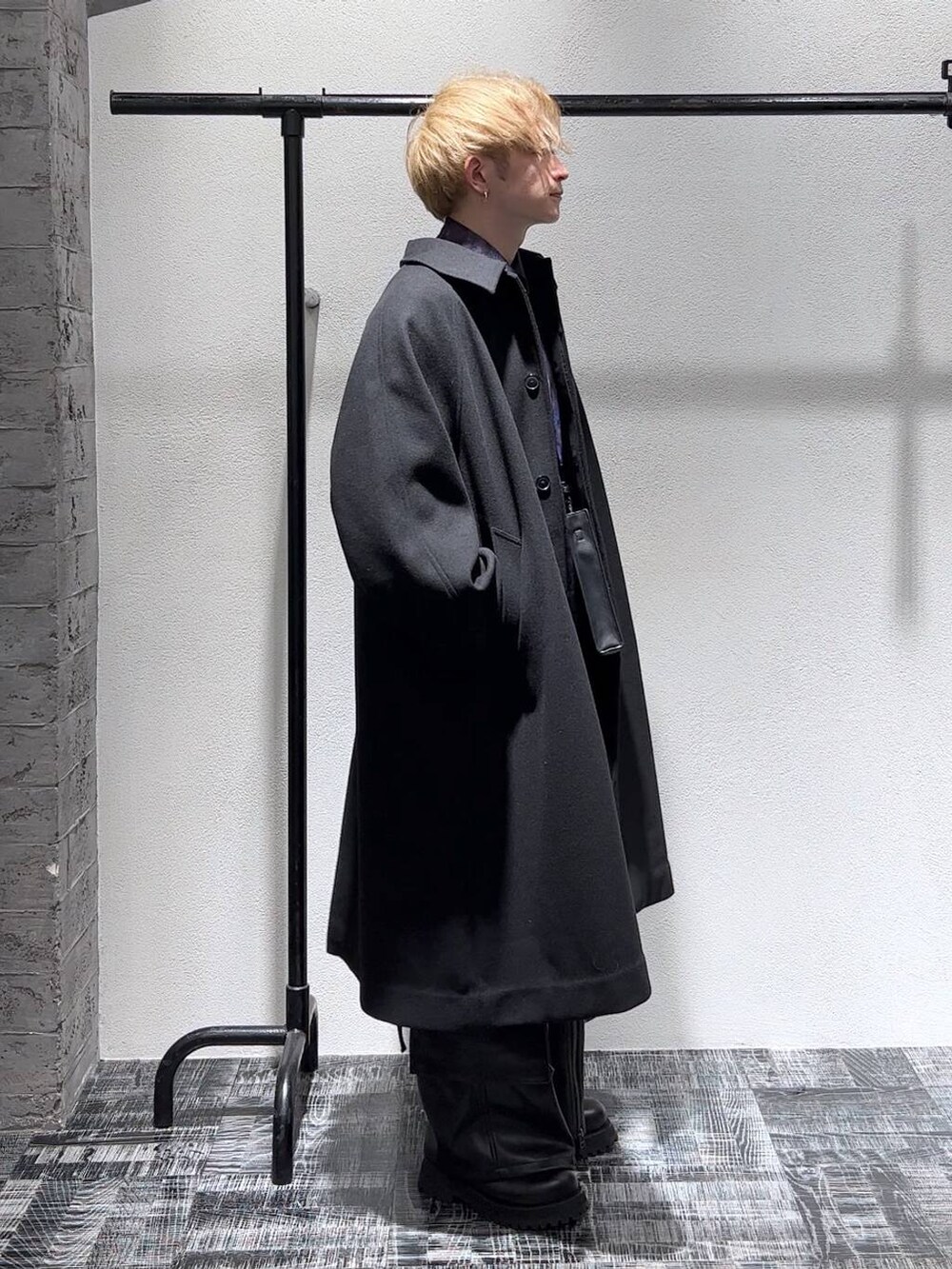 ブラック系のステンカラーコート、ブラック系のショルダーバッグ、ブラック系のブーツを着用したメンズの秋コーディネートの4枚目の写真