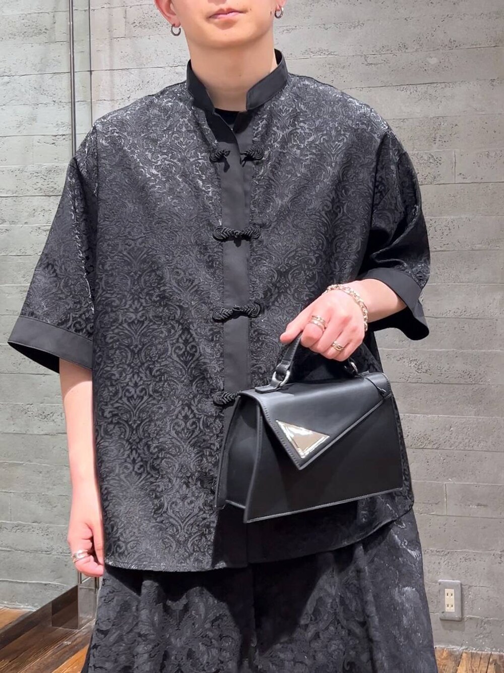 ブラック系のスラックス、ブラック系のハンドバッグ、ブラック系のサンダルを着用したメンズの夏コーディネートの5枚目の写真