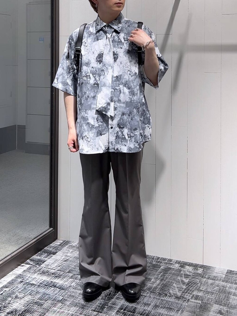 ブラック系のドレスシューズ、ブラック系のショルダーバッグ、グレー系のスラックスを着用したメンズの春コーディネートの2枚目の写真