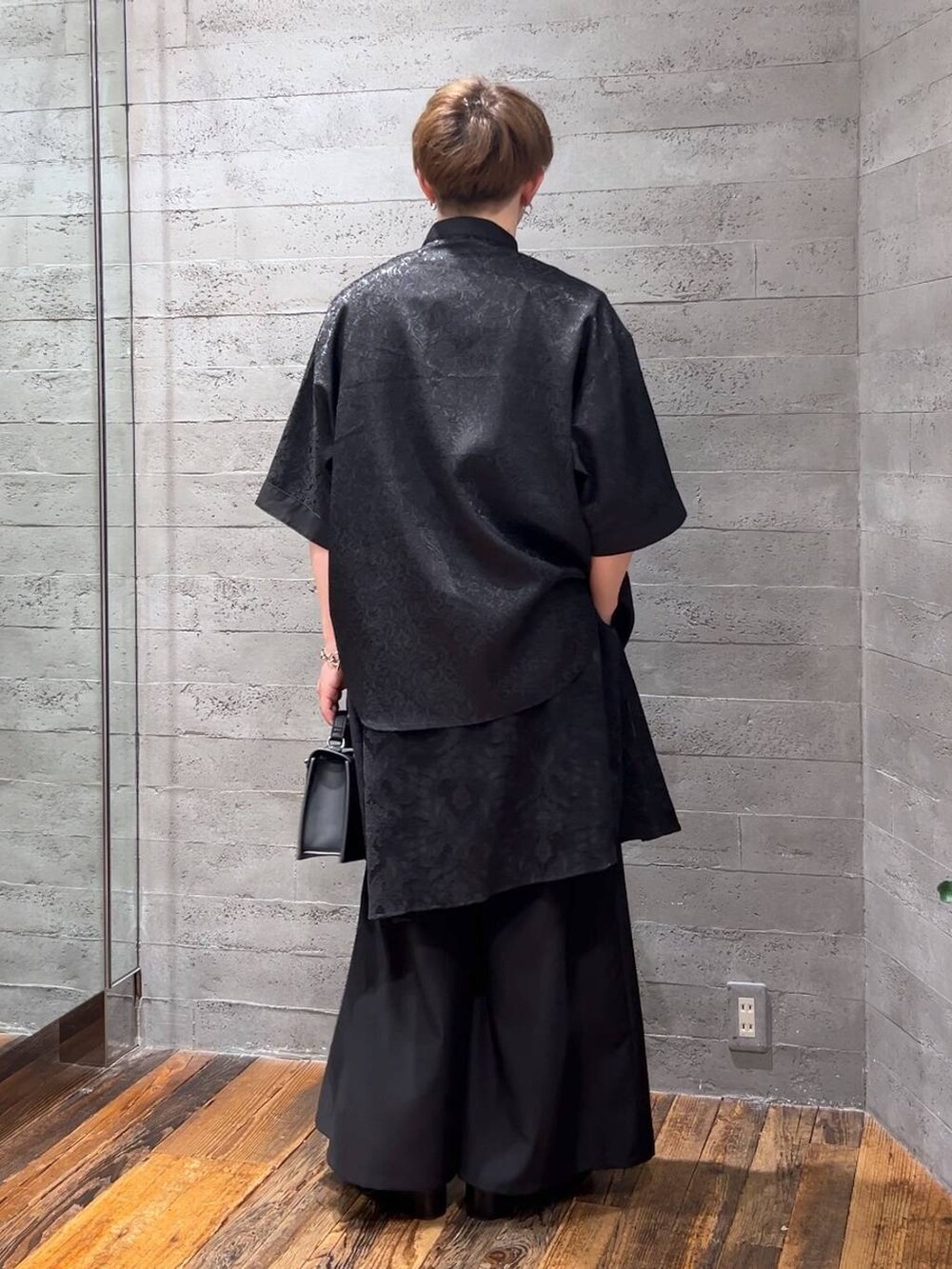 ブラック系のスラックス、ブラック系のハンドバッグ、ブラック系のサンダルを着用したメンズの夏コーディネートの3枚目の写真