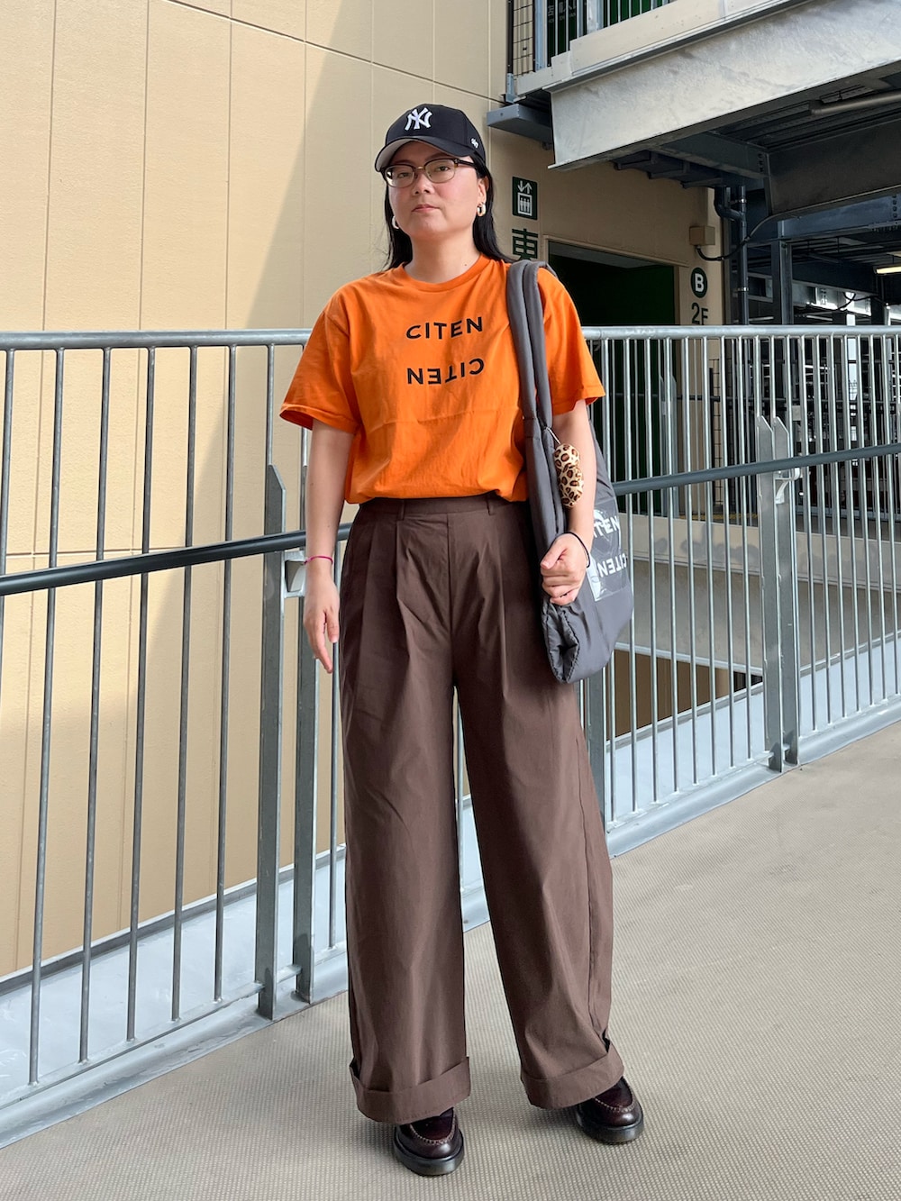 オレンジ系のTシャツ/カットソー、グレー系のトートバッグ、ブラウン系のその他パンツを着用したレディースの夏コーディネートの2枚目の写真