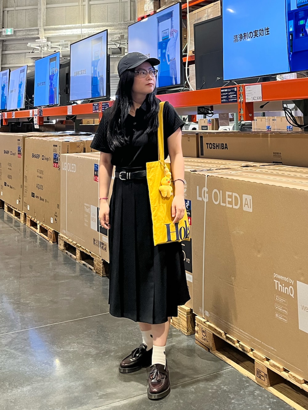 イエロー系のトートバッグ、ブラウン系のローファー、ブラック系のポロシャツを着用したレディースの夏コーディネートの2枚目の写真