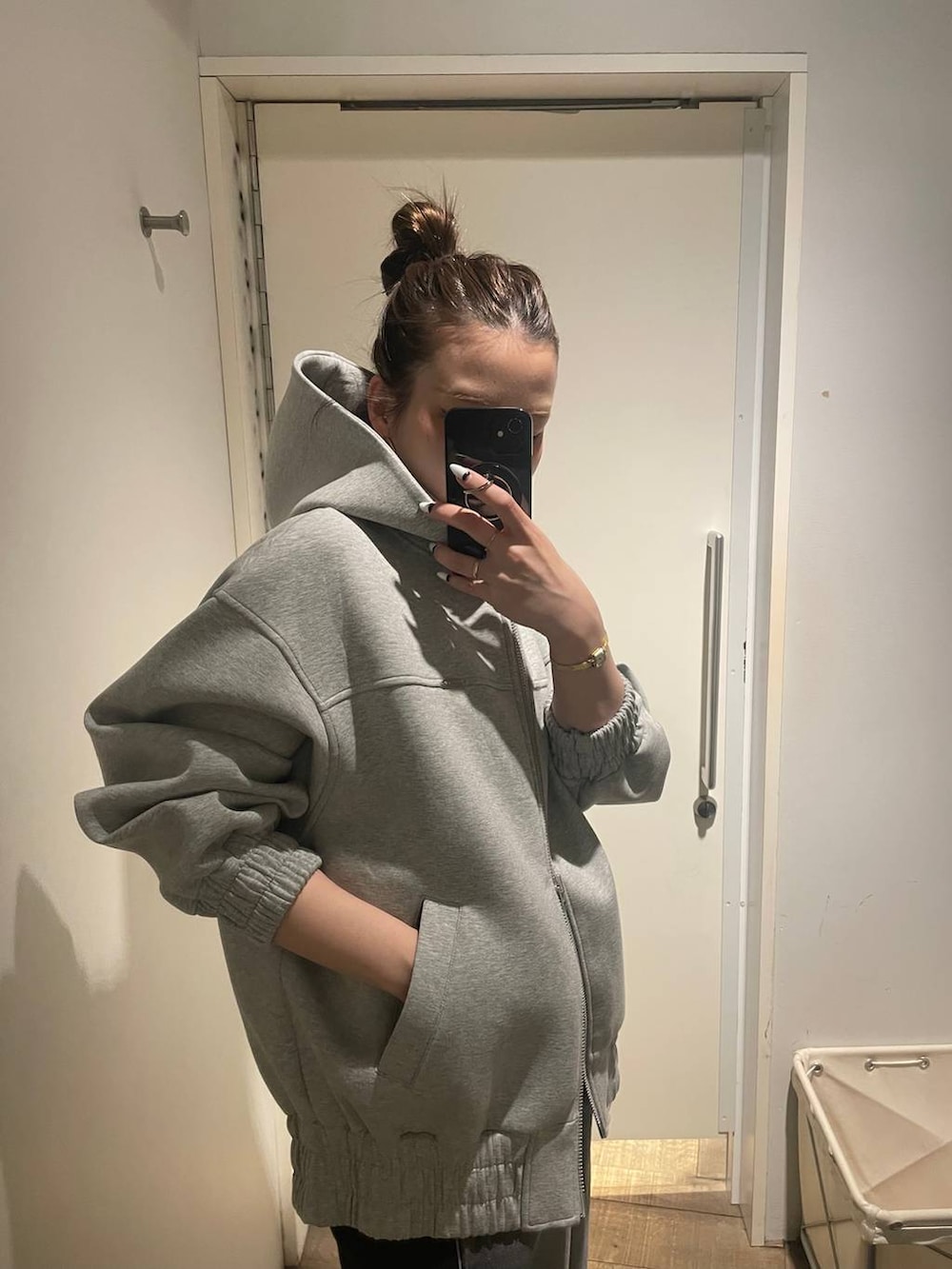 グレー系のパーカー、ブラック系のデニムパンツ、ゴールド系のピアス（両耳用）を着用したレディースの冬コーディネートの4枚目の写真