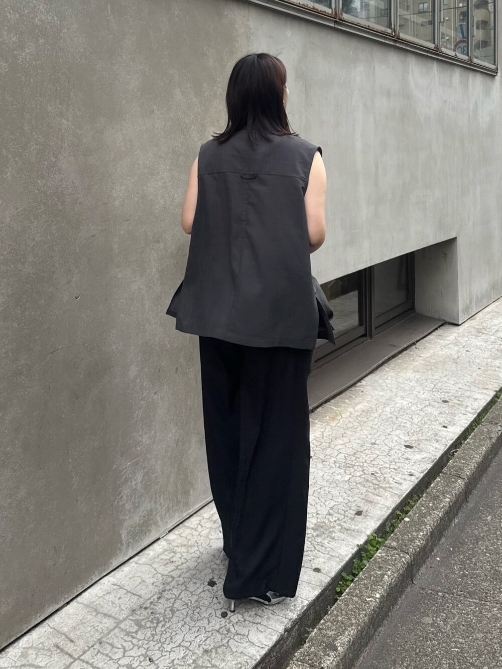 グレー系のベスト、グリーン系のタンクトップ、ブラック系のスラックスを着用したレディースの夏コーディネートの2枚目の写真