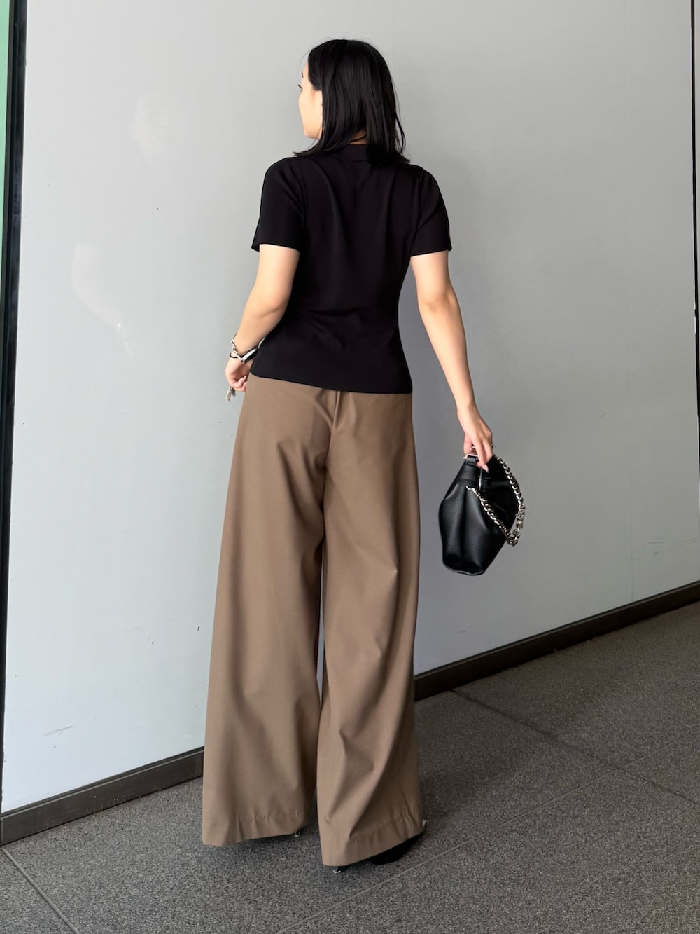 ブラック系のTシャツ/カットソー、ブラウン系のスラックス、ブラック系のトートバッグを着用したレディースの春コーディネートの2枚目の写真