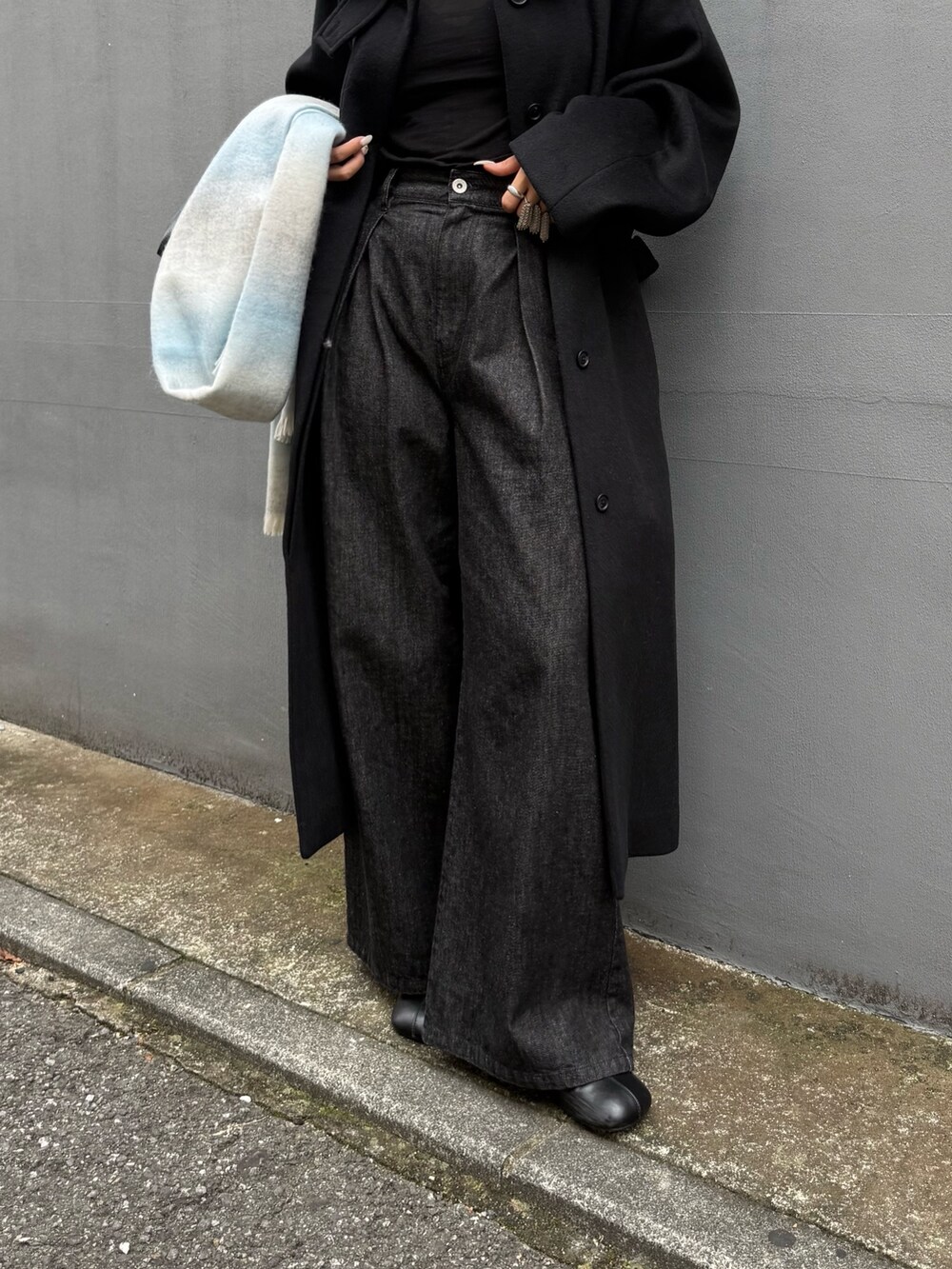 ブラック系のチェスターコート、ブラック系のトートバッグ、ブラック系のデニムパンツを着用したレディースの秋コーディネートの4枚目の写真