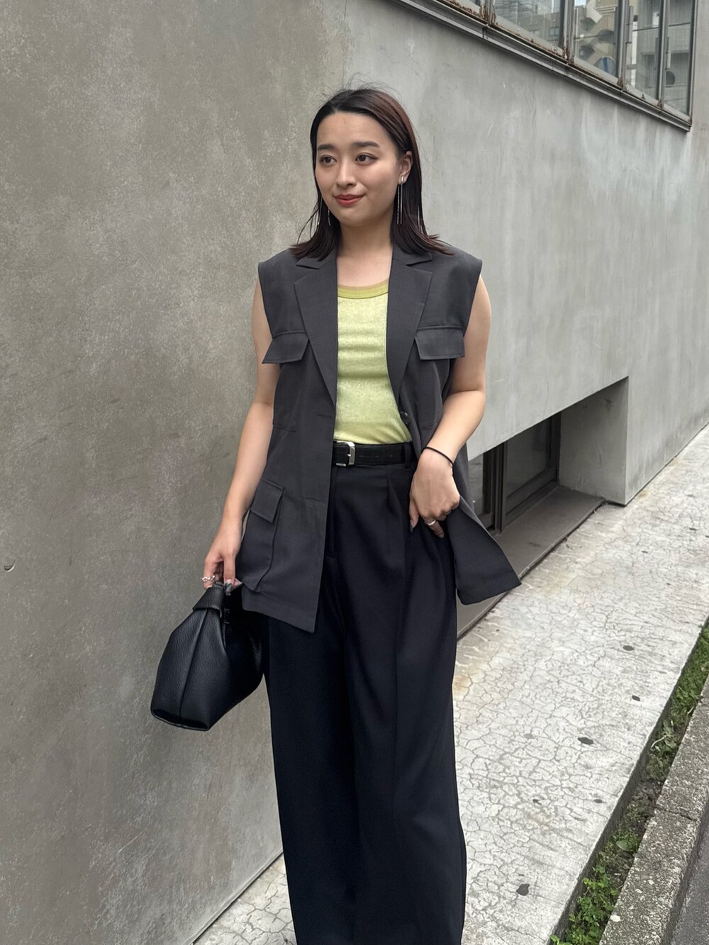 グレー系のベスト、グリーン系のタンクトップ、ブラック系のスラックスを着用したレディースの夏コーディネートの3枚目の写真