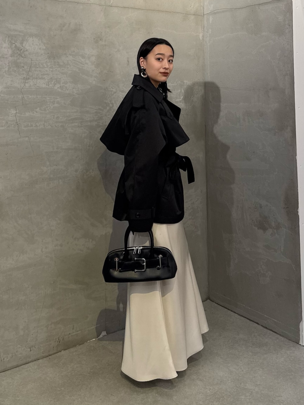 ブラック系のトレンチコート、ホワイト系のスカート、ブラック系のショルダーバッグを着用したレディースの冬コーディネートの2枚目の写真