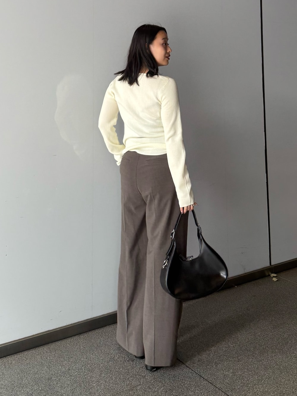 ホワイト系のニット/セーター、ブラウン系のスラックス、ブラック系のブーツを着用したレディースの夏コーディネートの2枚目の写真